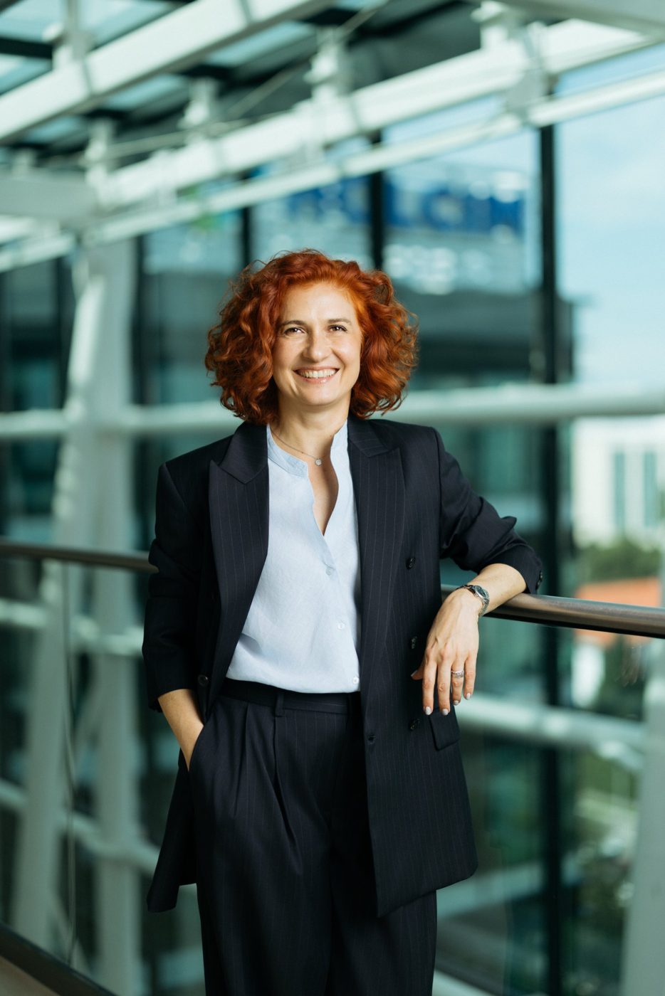 Portret corporate al unei femei în costum, sprijinită de o balustradă într-o clădire de birouri